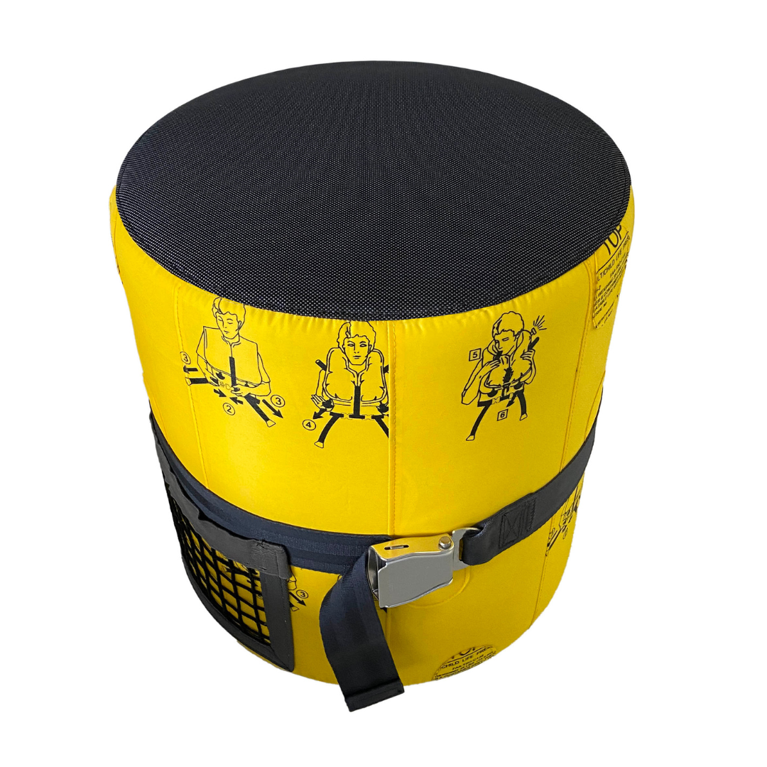 Gelbes Sicherheitsgerät mit schwarzem Deckel und blauer Gurtschnalle, bebilderte Anleitung in Schwarz, seitliche Netztasche