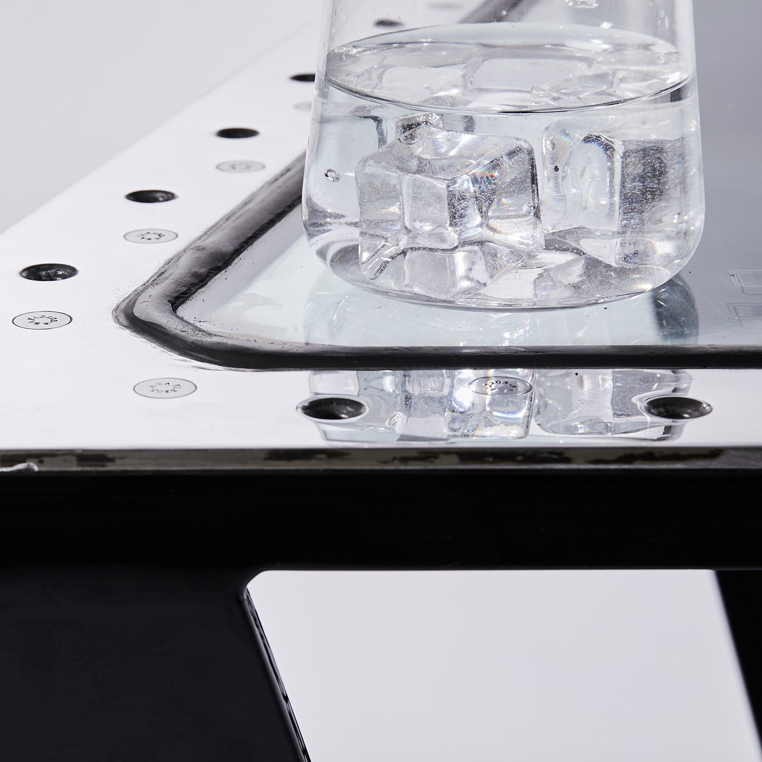 Transparenter Glasbehälter mit Wasser und Eiswürfeln auf reflektierender Metalloberfläche