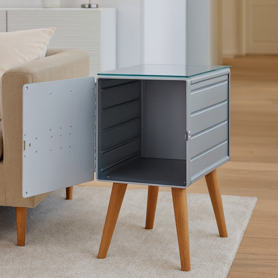 Kleiner grauer Metallschrank mit offener Tür, vier Holzbeinen auf hellem Teppich.