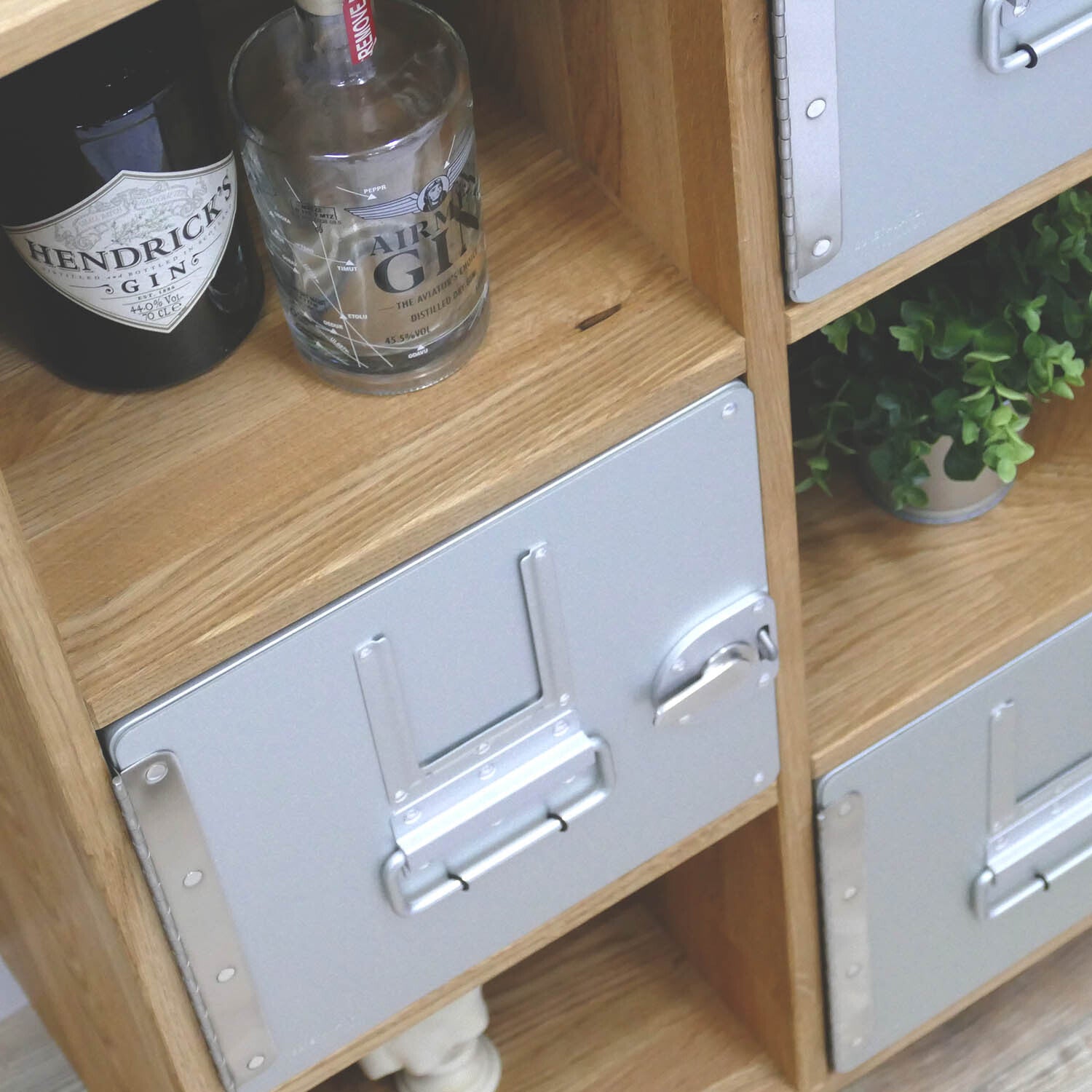 Hochwertiges Holzregal mit Metallfrontschubladen, neben Hendrick's und Air Ministry Gin Flaschen.