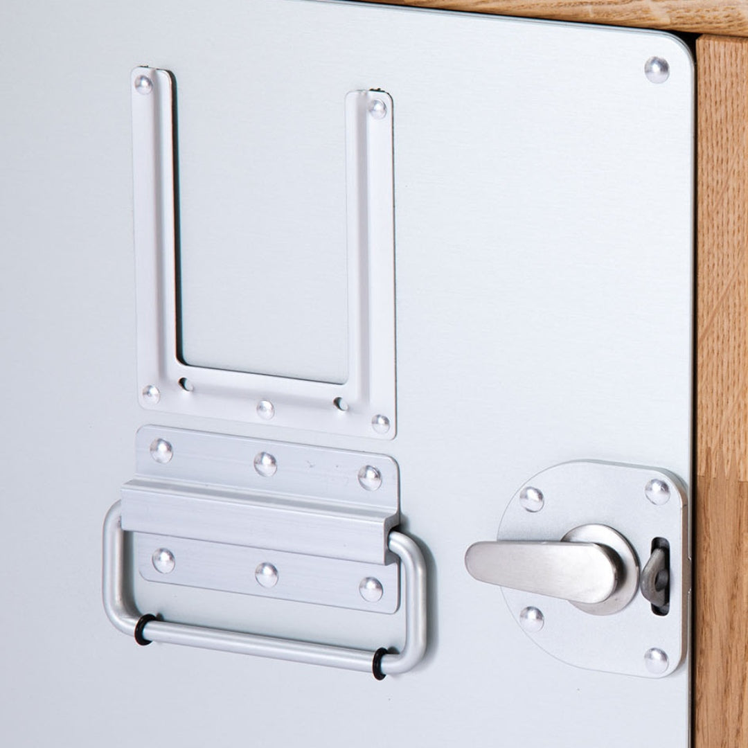 Nahaufnahme eines Metallpaneels mit silbernem Griff, Riegelverschluss und U-förmiger Halterung auf hellbraunem Holz.