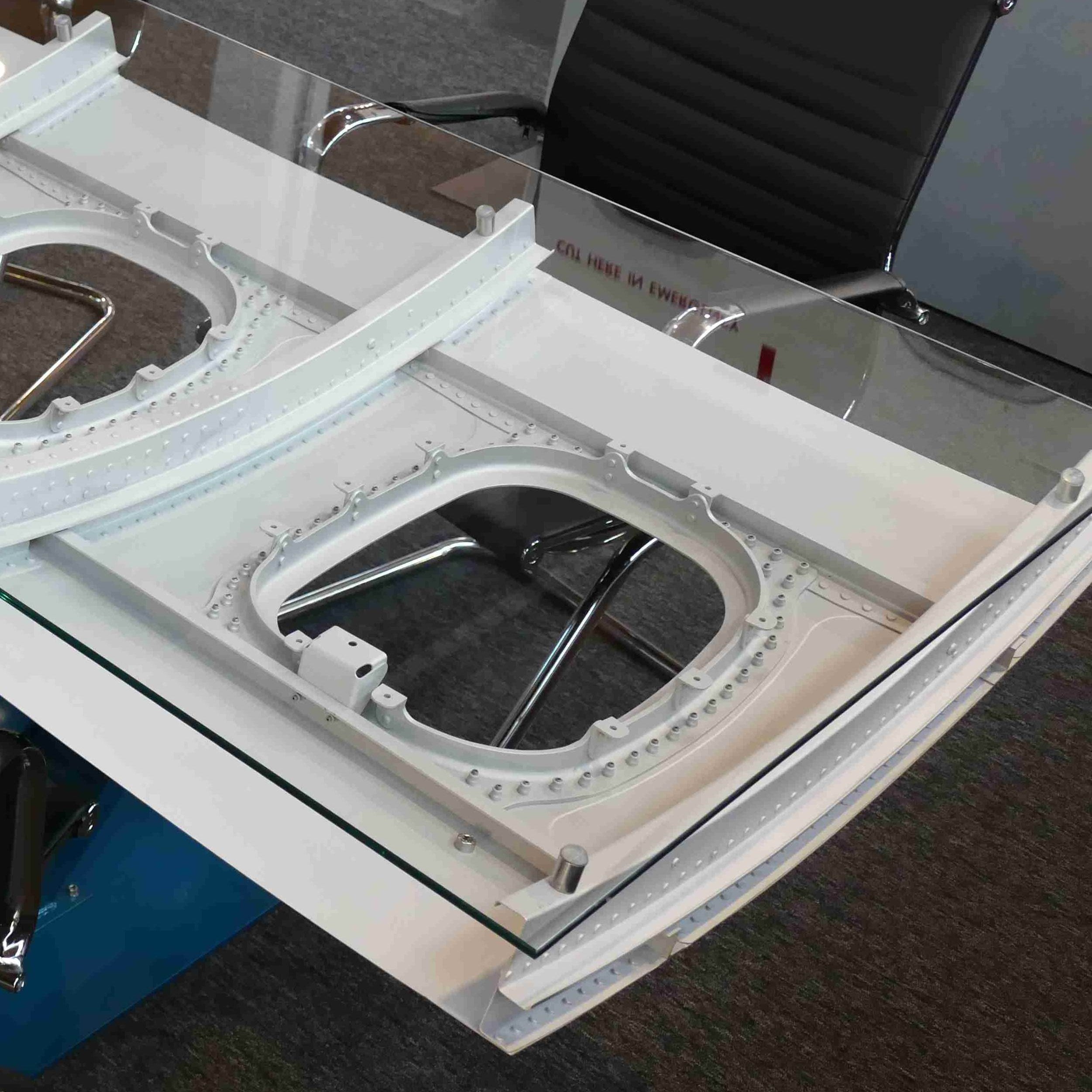 Moderner Bürotisch mit Glasplatte und weißen Metallstrukturen, schwarzer ergonomischer Bürostuhl, graue Trennwand.