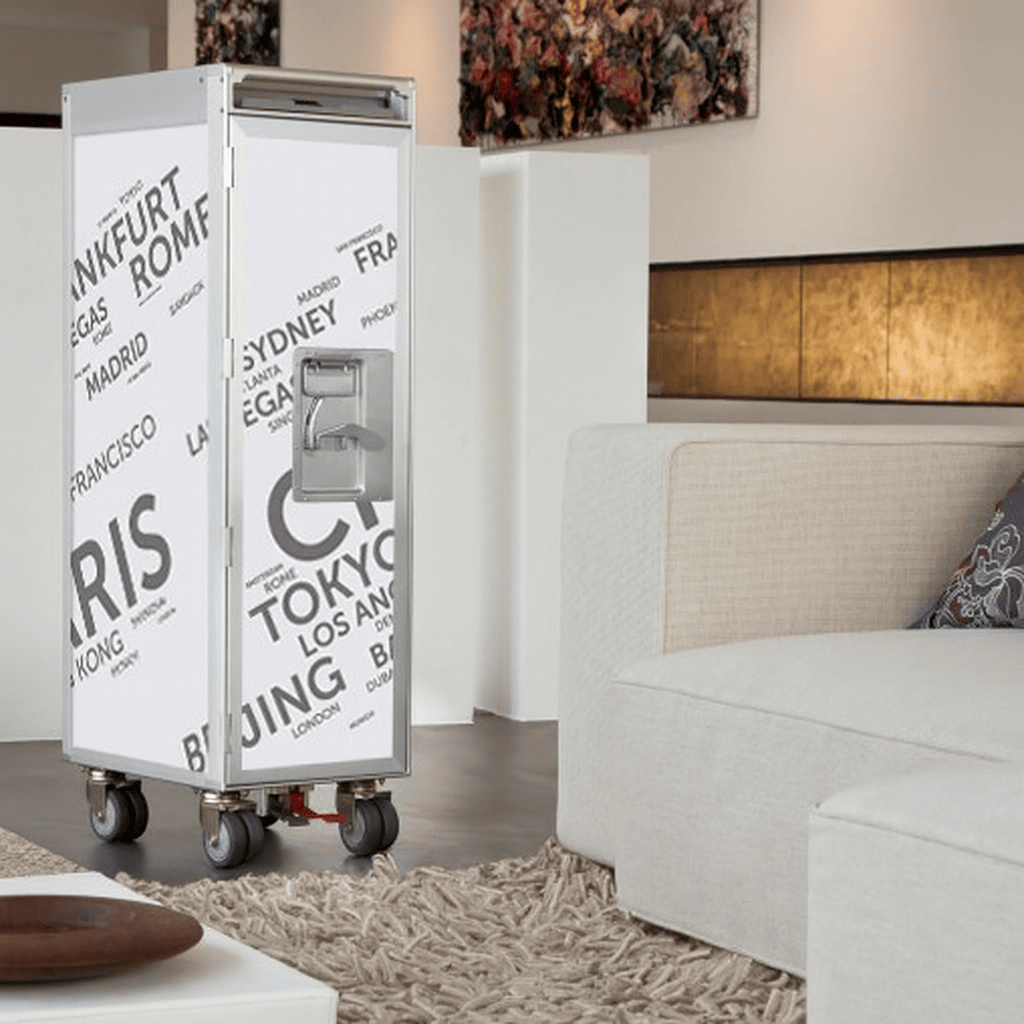 Moderner Wohnraum mit beigem Ecksofa, flauschigem Teppich und weißem, rollbarem Aufbewahrungswagen mit Städtenamen-Dekor