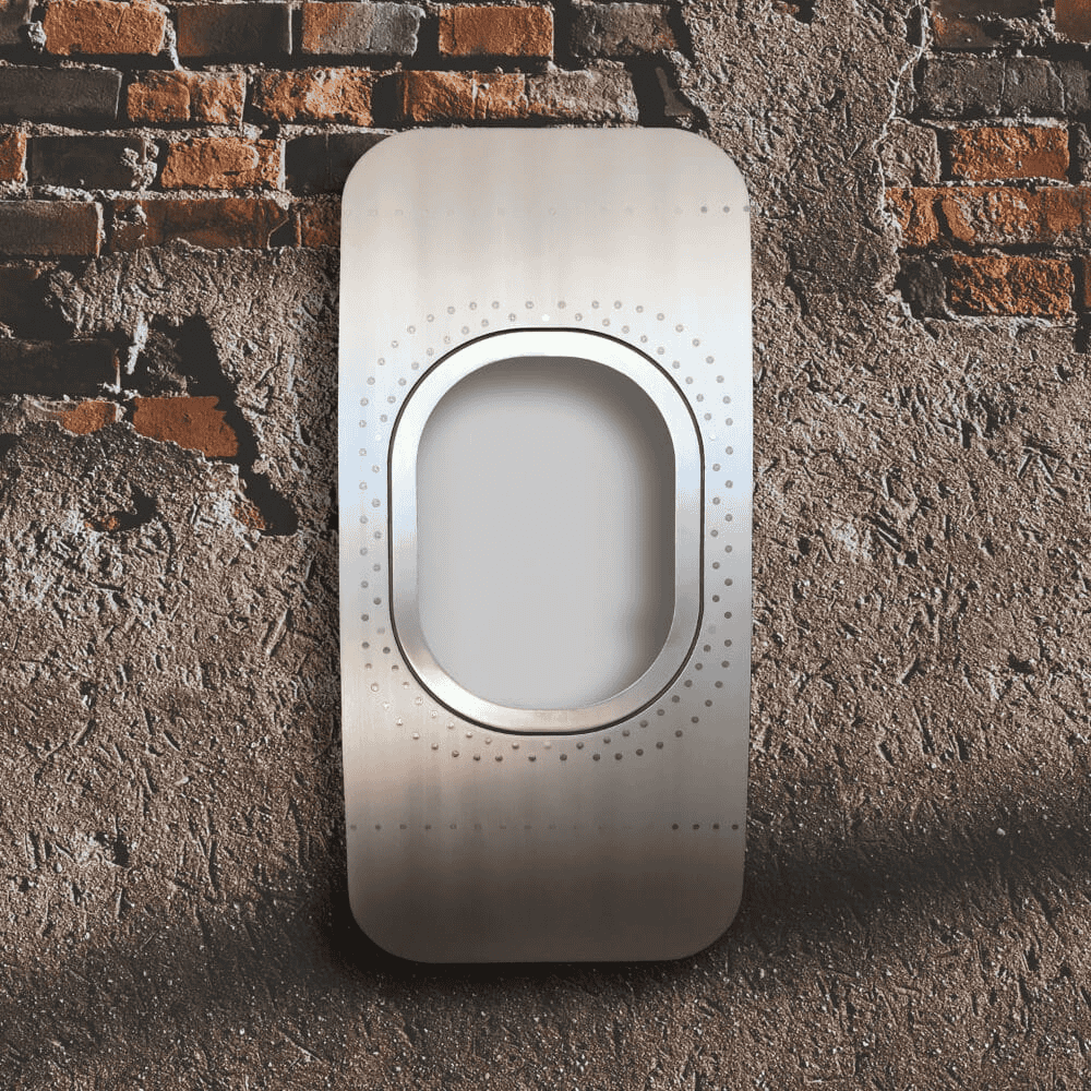 Modernes, glänzendes Metallpaneel mit ovalem Ausschnitt und dekorativen Punktkreisen an roher Backstein- und Betonwand.