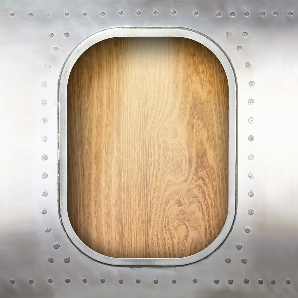 Ovales Metallfenster mit Nieten, das eine Holzplatte mit Maserung zeigt.