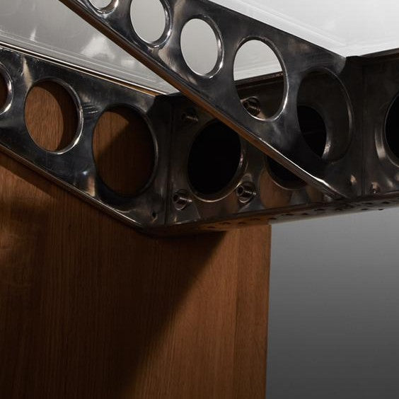 Polierter Metallhalter mit kreisförmigen Ausschnitten zwischen vertikaler Holzplatte und hellem Deckenelement