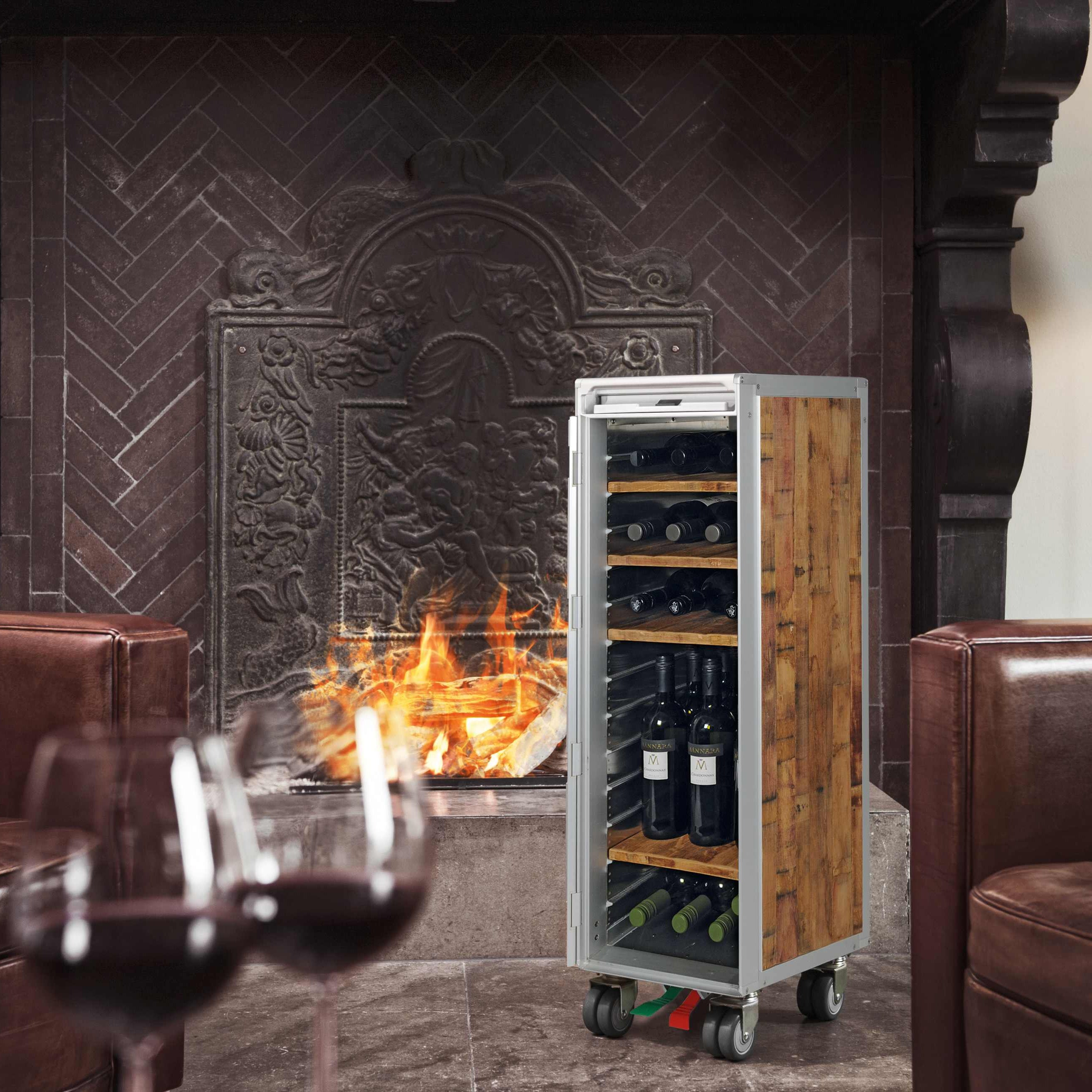 Moderner Weinlagerschrank neben einem brennenden Kamin mit zwei Ledersesseln und Rotweingläsern im Vordergrund.