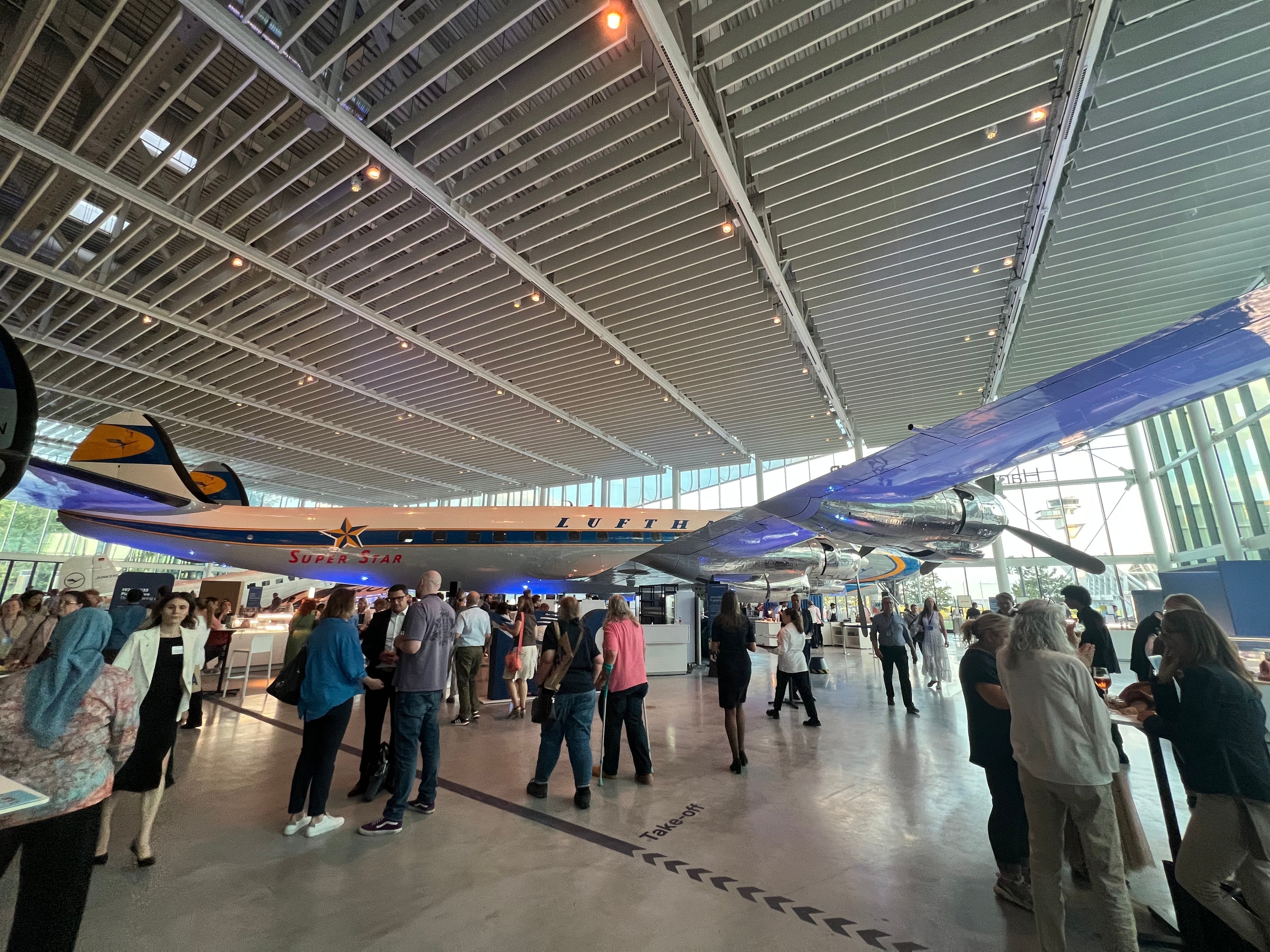 Attendees networking beneath a historic Lufthansa Lockheed Super Star aircraft at the Lufthansa Group Roadshow in Frankfurt