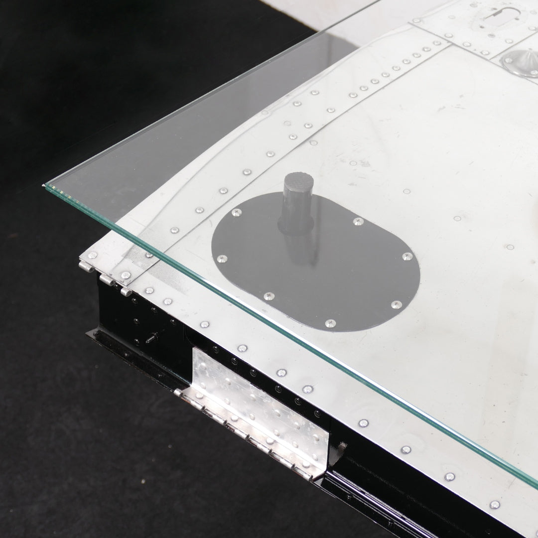 Moderner Designer-Glas-Tisch mit Edelstahlgestell und sichtbaren Nieten, inspiriert von Flugzeugtechnik.