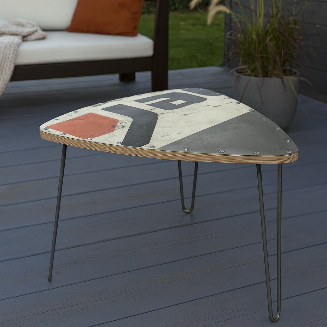 Dreieckiger Außentisch mit rustikalem Holz-Metall-Deckel, Schriftzug 'Yard', gepolsterter Bank und Ziergras.