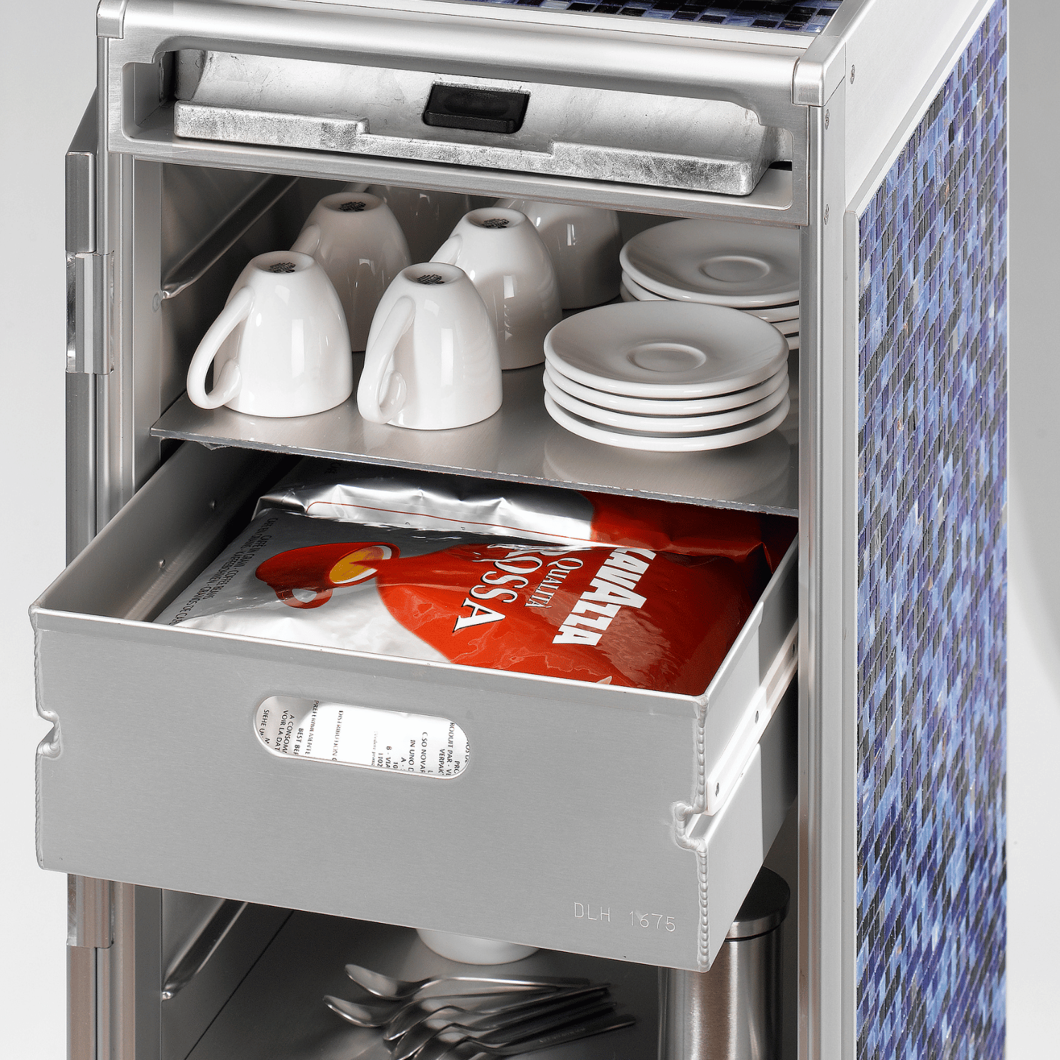 Geöffneter Edelstahlschrank mit weißen Porzellantassen, ausgezogenem Metallfach mit Kaffeepaket und blauem Mosaikmuster.