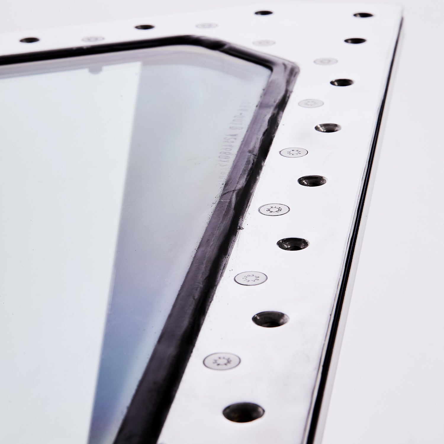 Nahaufnahme einer Flugzeugfensterecke mit Metallrahmen, schwarzen Dichtungen, Nieten und Gravur.