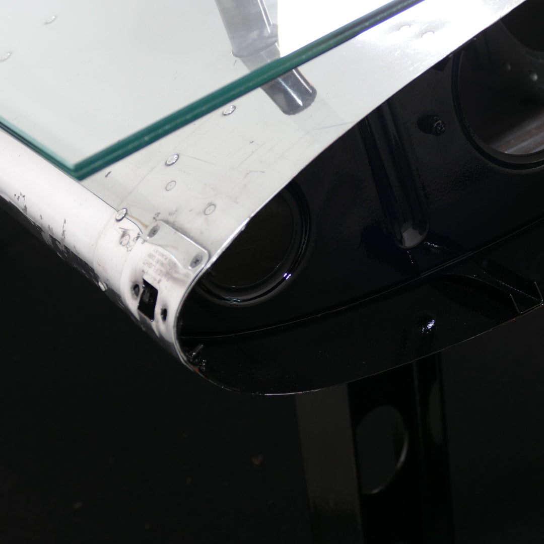 Nahaufnahme eines Flugzeugflügels mit genieteter Metalloberfläche und Glaselement.