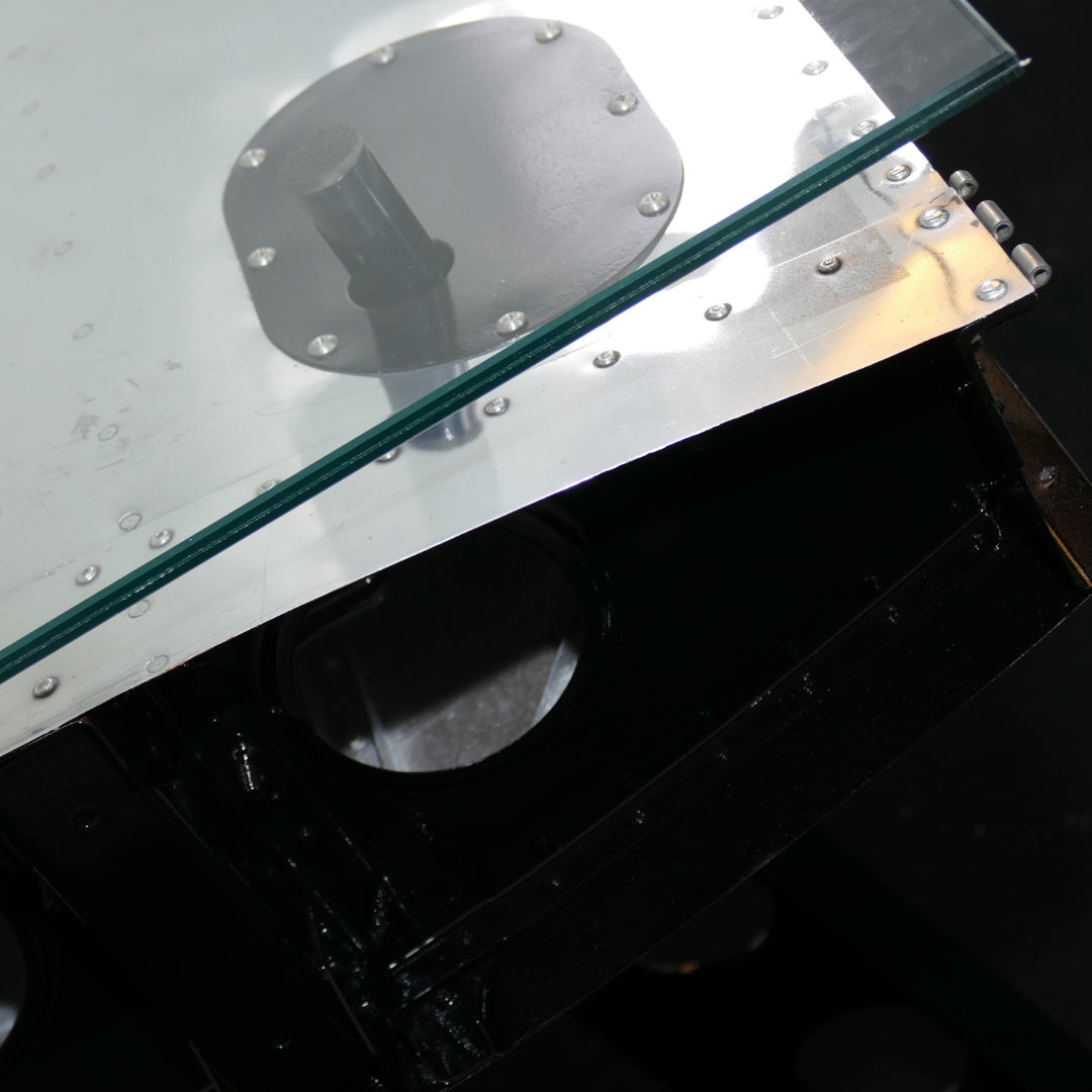 Nahaufnahme einer Glasscheibe mit Metallnieten und schwarzem Metallrahmen mit runder Öffnung.