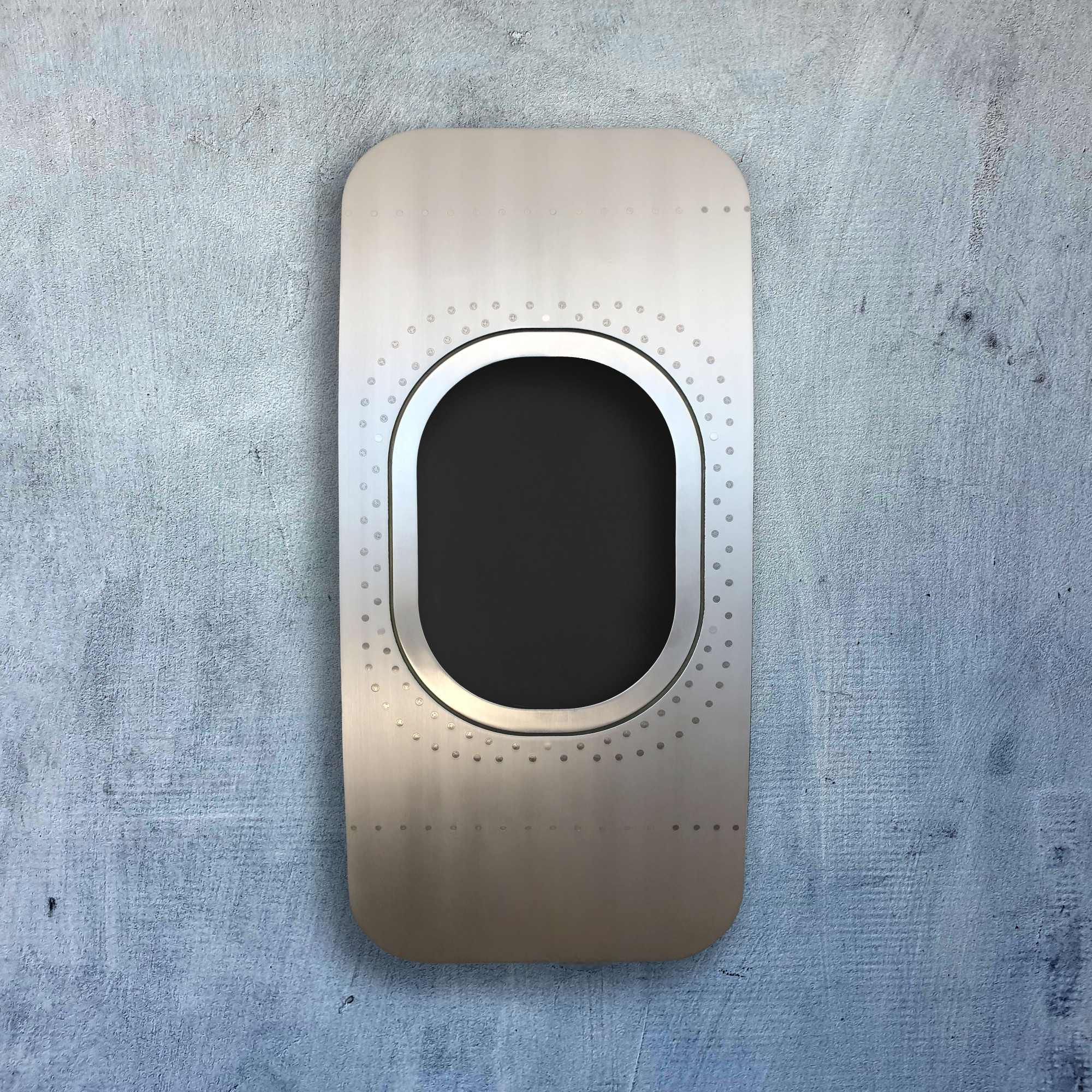 Metallpaneel mit ovalem schwarzen Fenster und Nieten auf blau-grauer Wand