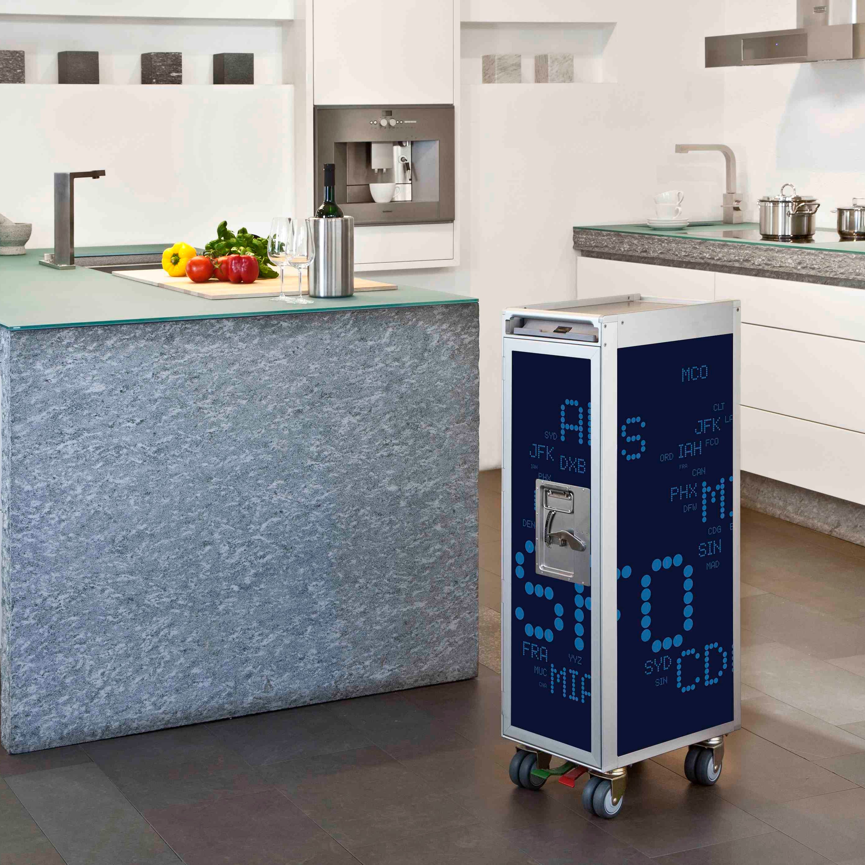 Moderner Küchenraum mit rollbarem Metallwagen und blauen Flughafencodes neben Kücheninsel mit Gemüse und Wein.