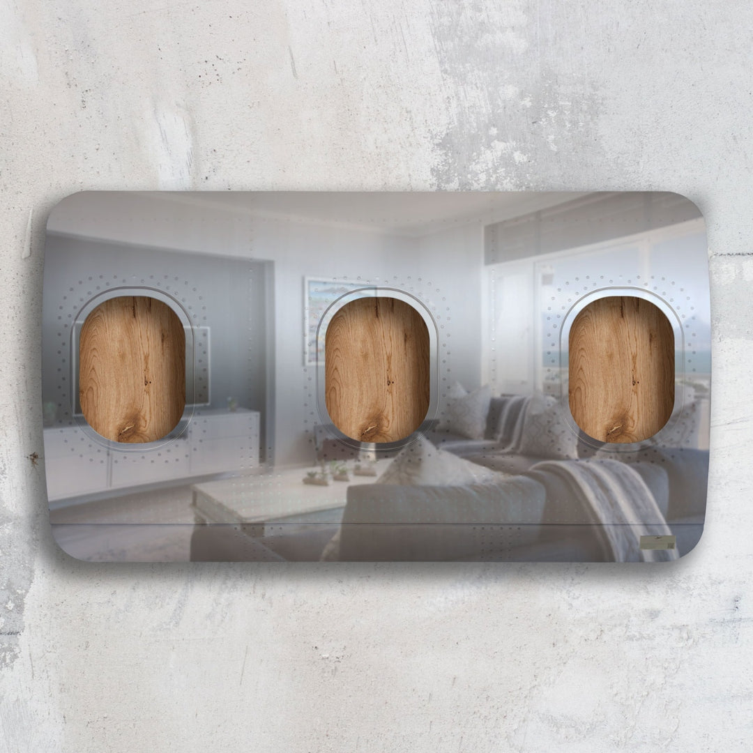 Moderner Lichtschalter mit drei hölzernen Kippschaltern in einem Wohnzimmer mit Sofa und Meerblick.