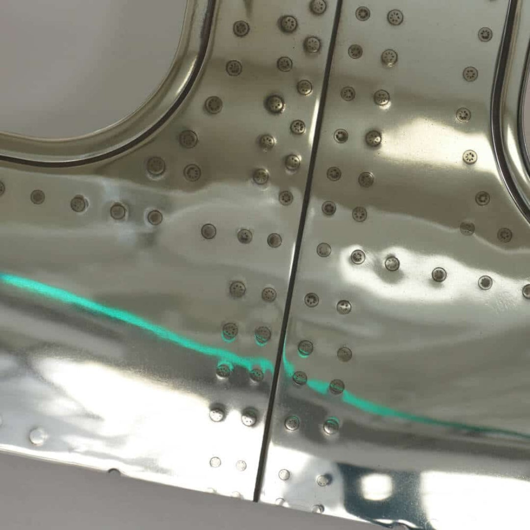 Nahaufnahme einer glänzenden metallischen Oberfläche mit runden Nieten und türkisem Reflexionsstreifen