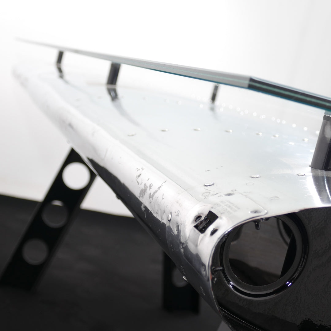 Polierter Flugzeugflügelabschnitt aus Metall mit Nieten, getragen von zwei schwarzen Ständern vor weißem Hintergrund