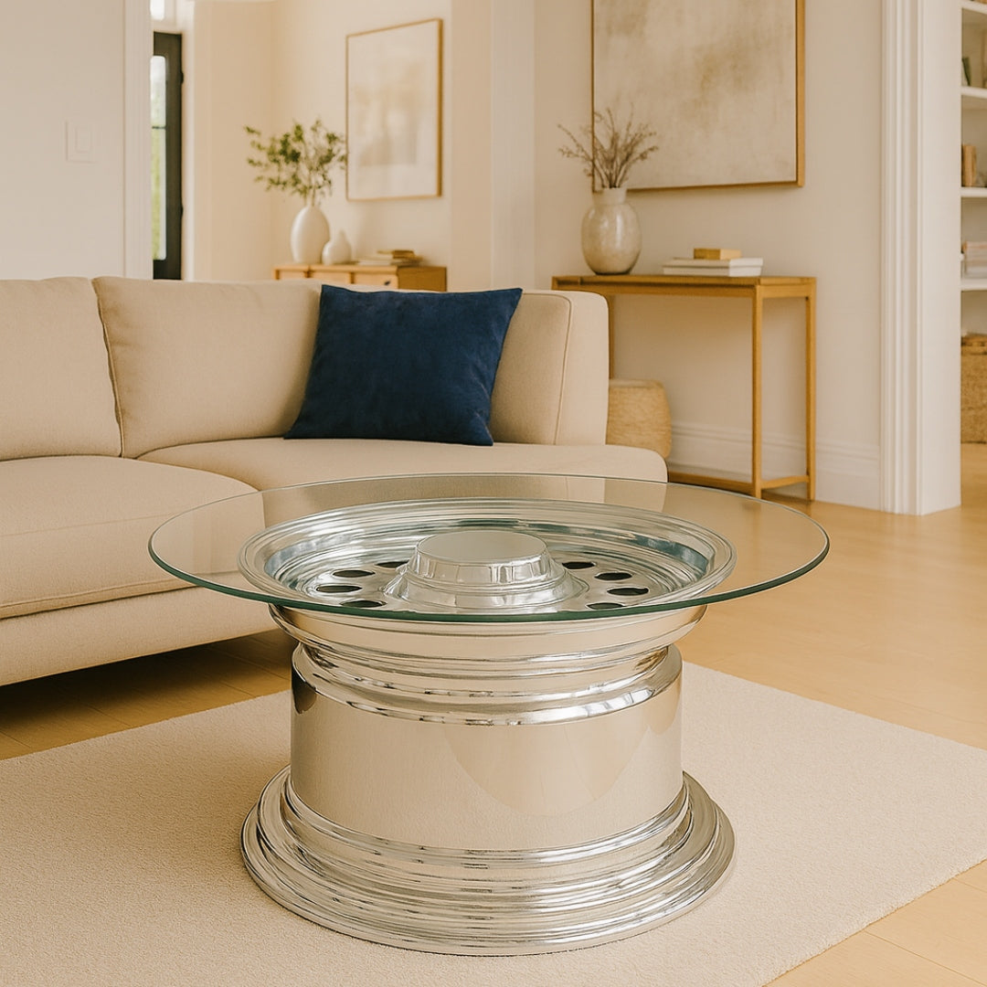 Moderner runder Couchtisch mit silbernem Radfelgenfuß und Glasplatte, beige Sofa und Holzkonsolen.